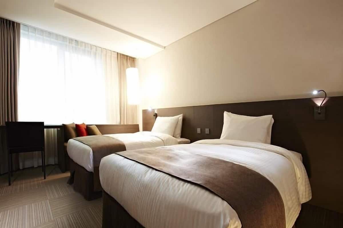 Une chambre d’hôtel avec deux lits, un bureau et une chaise.