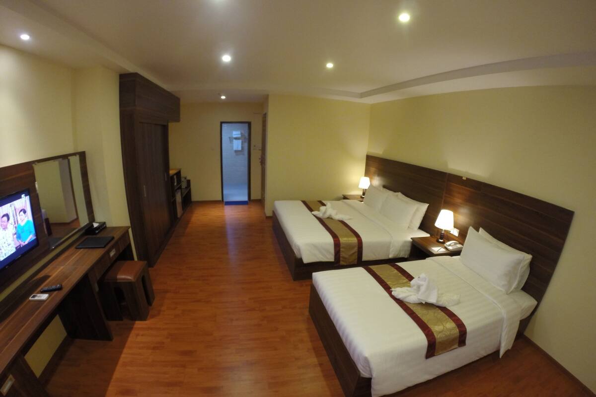 A hotel room with two beds, a desk with a television, and a mirror.