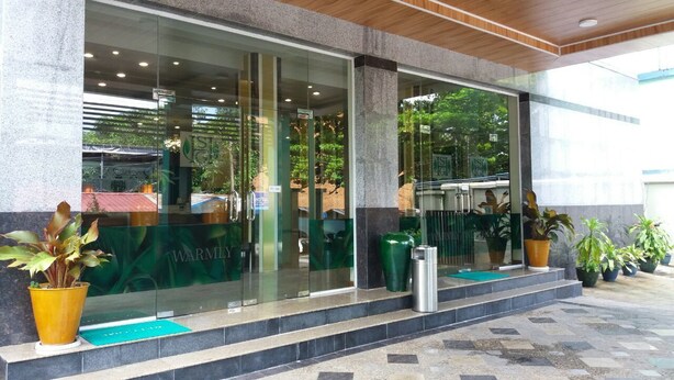Una entrada moderna de edificio con puertas de vidrio, fachada de piedra y plantas en macetas.