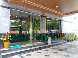Una entrada moderna de edificio con puertas de vidrio, fachada de piedra y plantas en macetas.