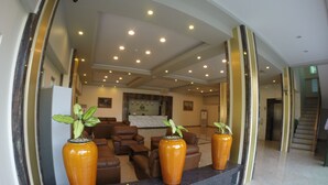 Un hall con mostrador de recepción, asientos de cuero y tres grandes jarrones con plantas.