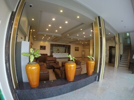 Un hall con mostrador de recepción, asientos de cuero y tres grandes jarrones con plantas.