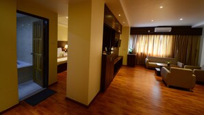 Una habitación de hotel con piso de madera, un sofá, una mesa de comedor y un televisor.