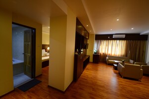 Una habitación de hotel con piso de madera, un sofá, una mesa de comedor y un televisor.