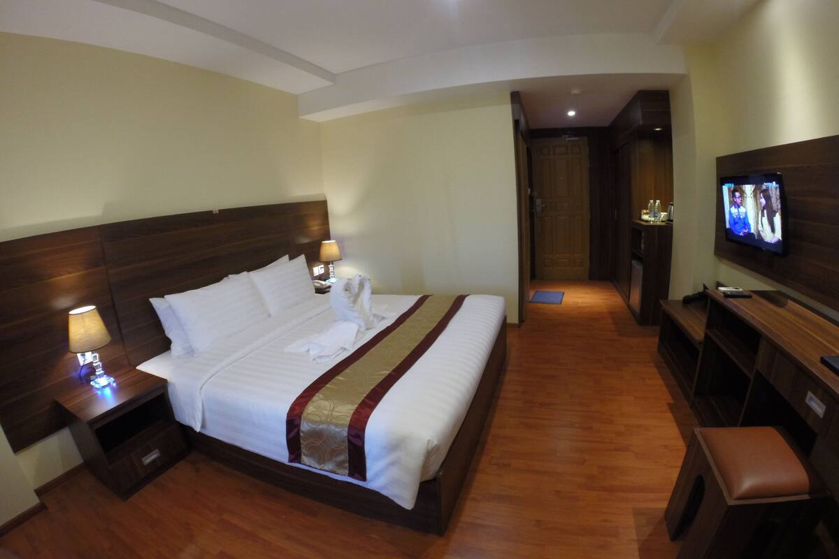 A hotel room with a large bed, a TV, a desk, and a wooden floor.
