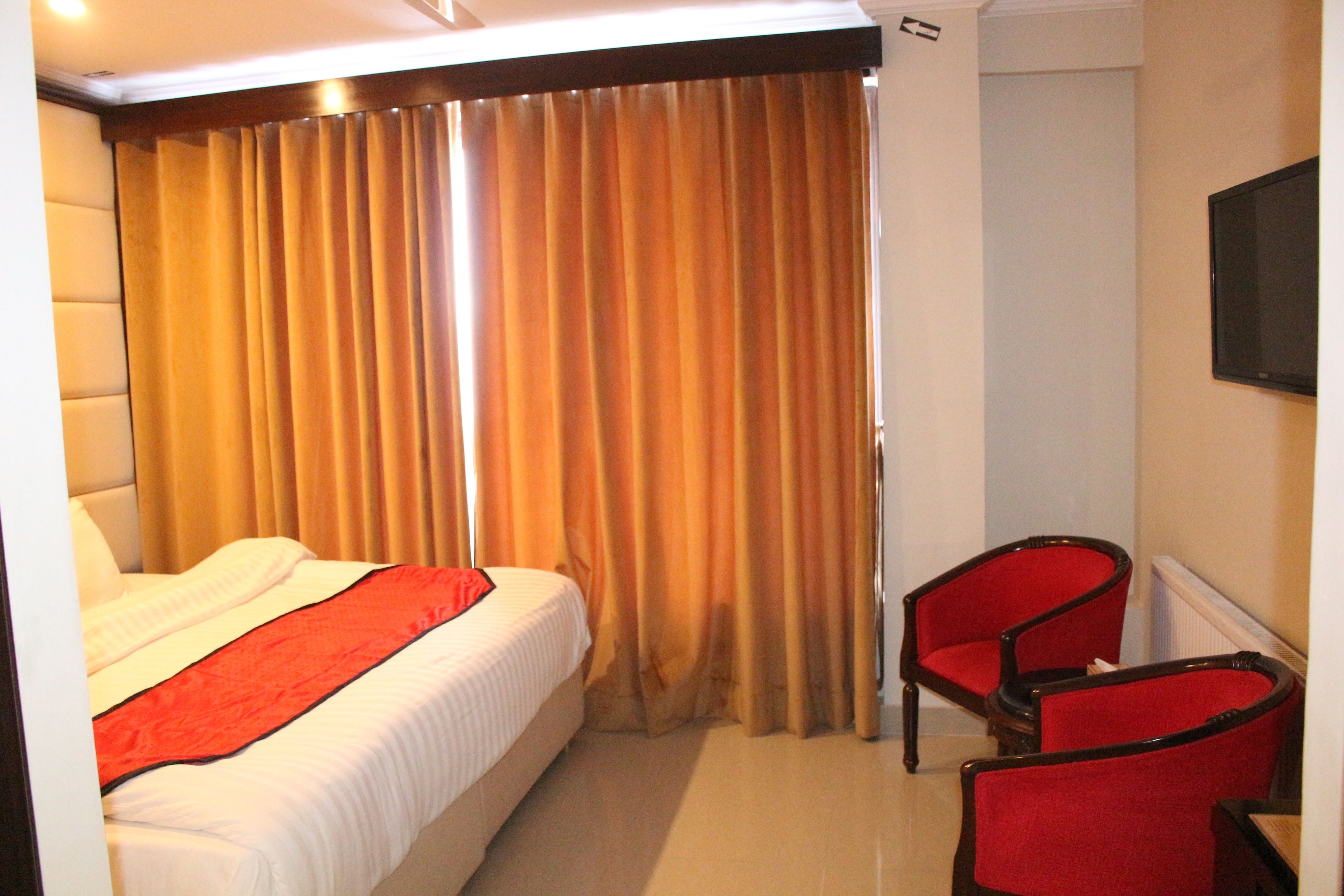 Una habitación de hotel con una cama, una silla roja y un televisor en la pared.