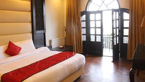 Habitación de hotel con una cama grande, una mesita de noche, un escritorio y vistas al exterior a través de un ventanal.