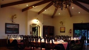 Un comedor con mesas y sillas de madera, una araña y obras de arte en las paredes.