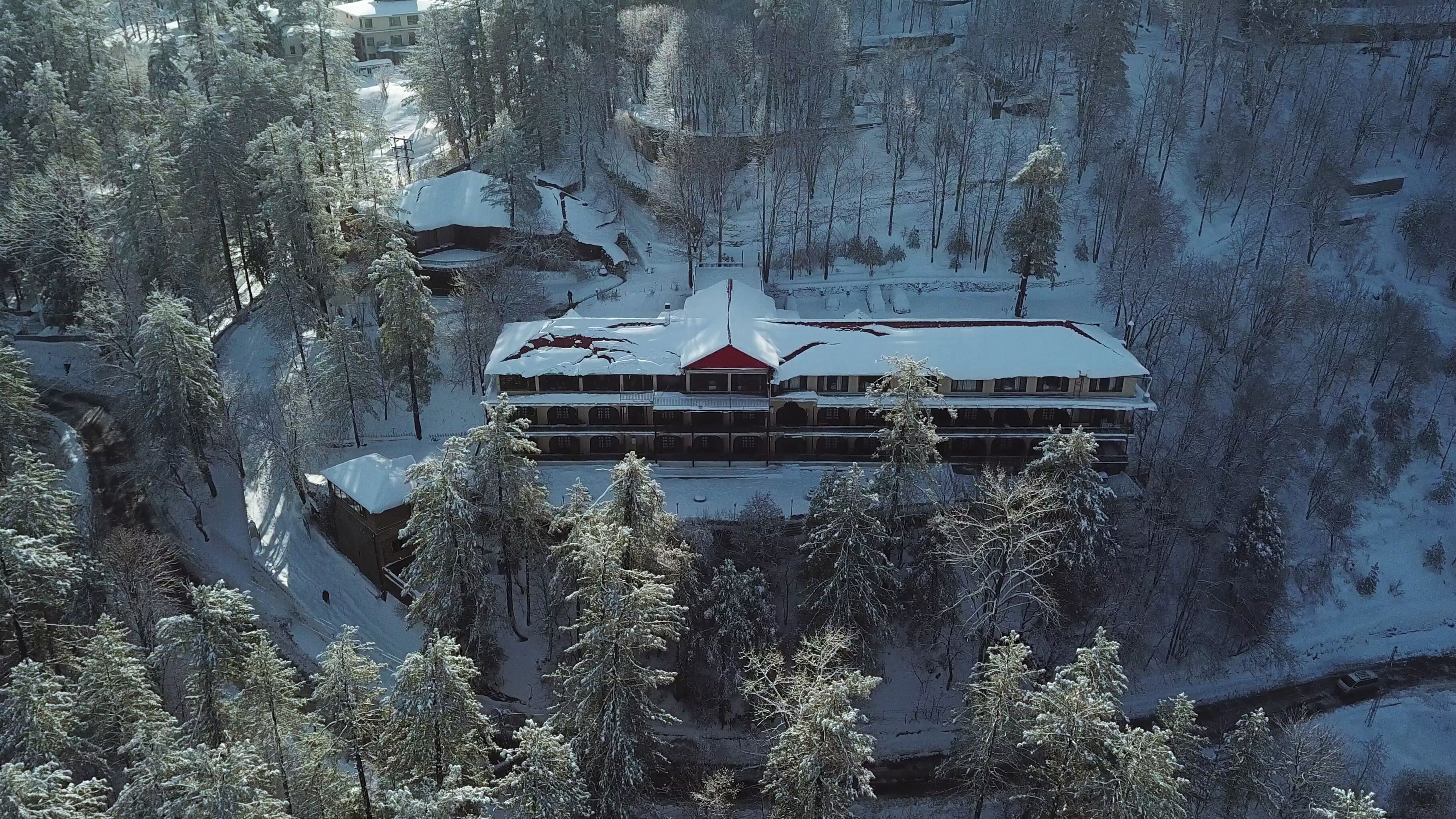 A multi-story building with a red roof, surrounded by snow-covered trees and a mountainous backdrop.