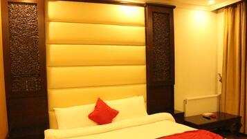 Una habitación de hotel con una cama grande, un cojín rojo, una mesita de noche de madera y un radiador.