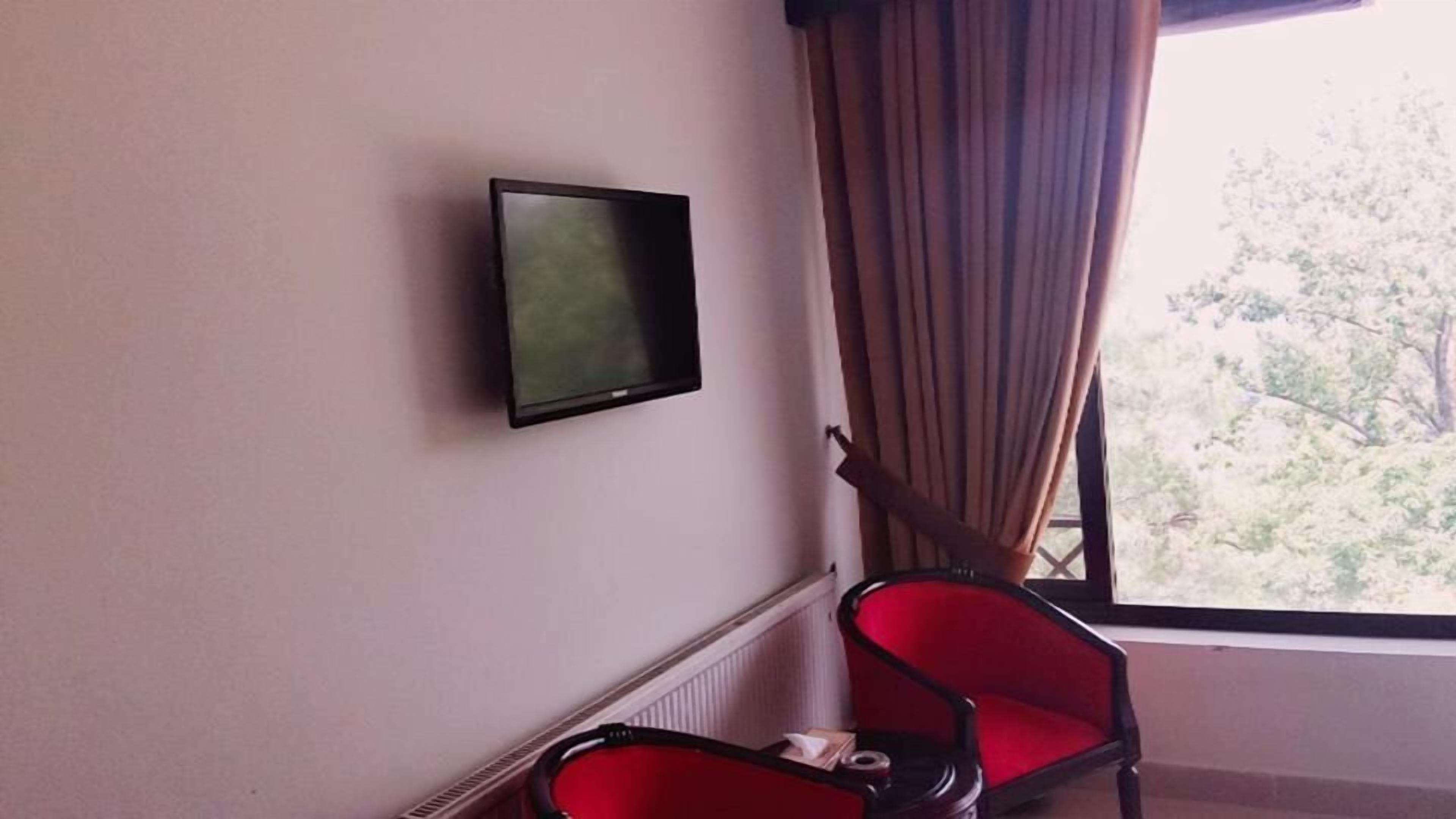A room with a television mounted on the wall, a red chair, and a window with curtains.