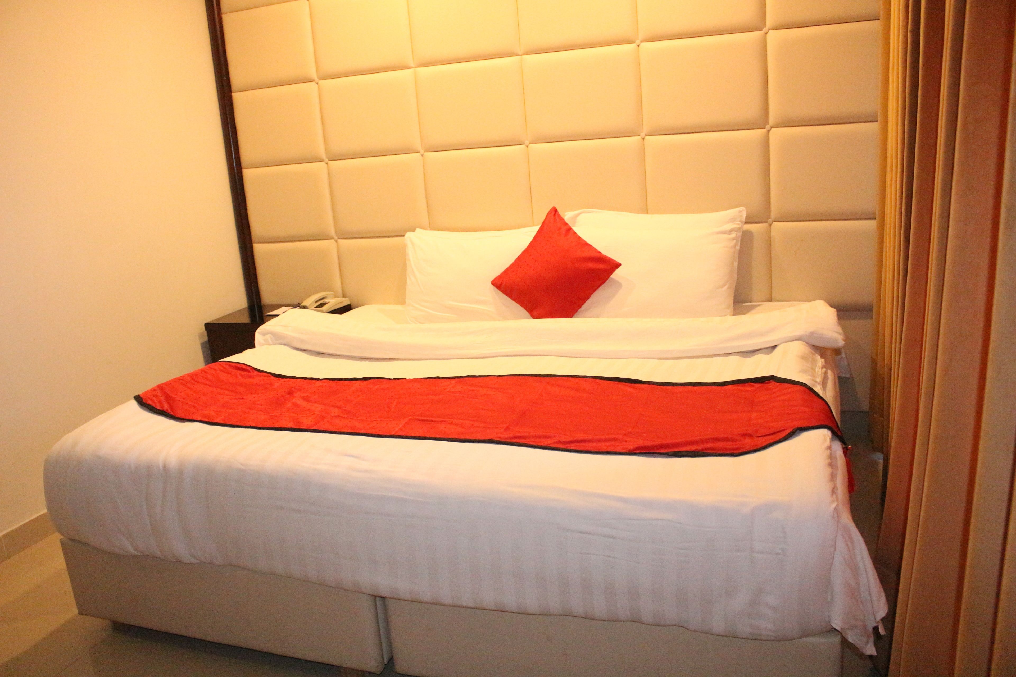Una cama bien hecha con un almohadón rojo, ropa de cama blanca y una manta roja.