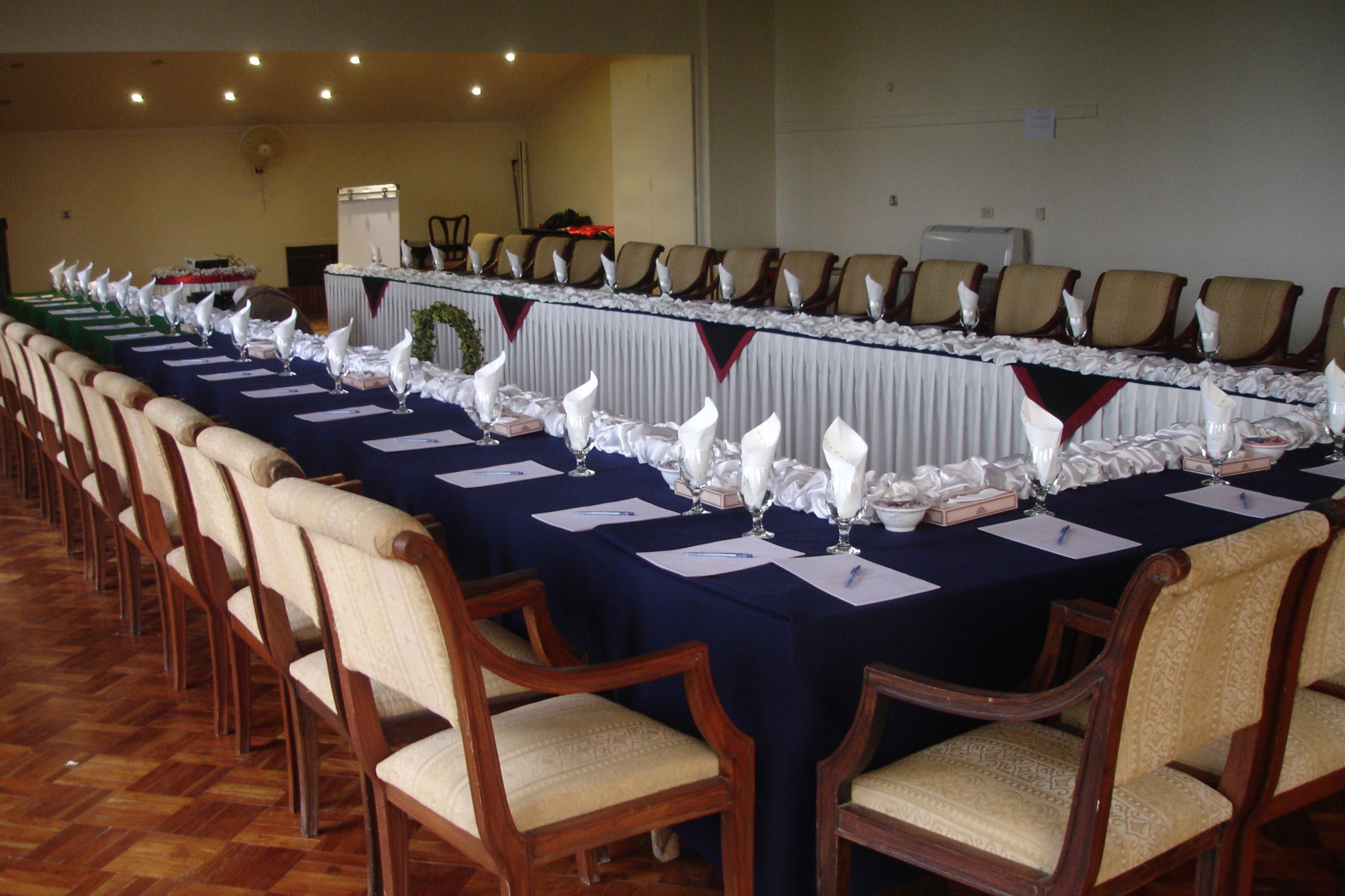 A conference room with a long table set for a meeting, surrounded by wooden chairs.