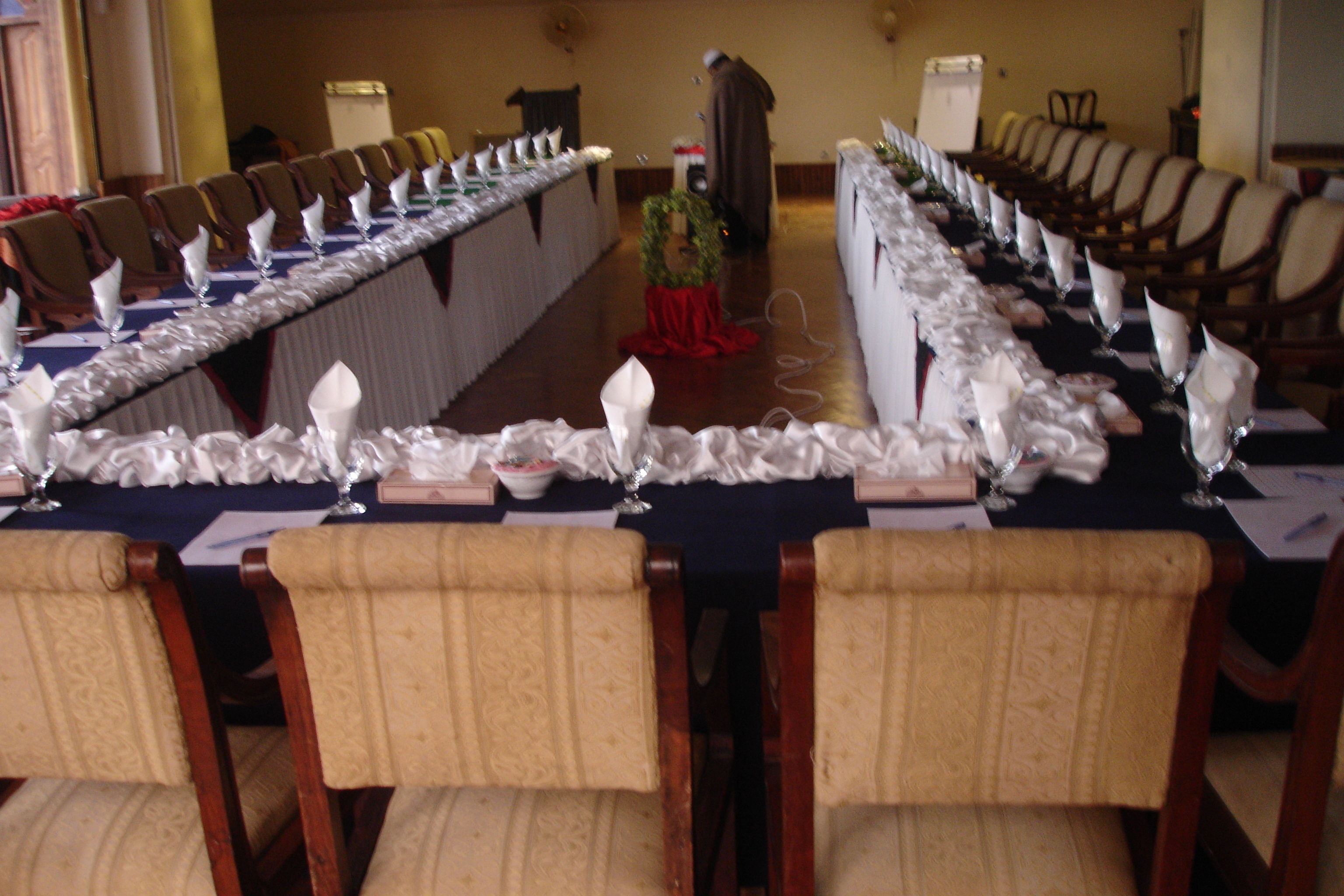 A long banquet table set for a formal event with rows of chairs and white tablecloths.