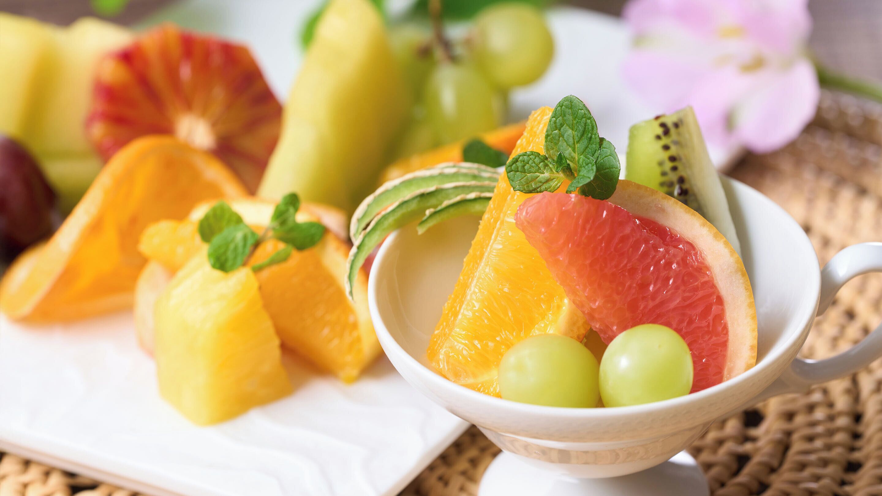 A bowl of assorted fruits including grapefruit, oranges, and kiwi, with mint leaves on top.