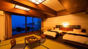 A hotel room with two beds, a sofa, a small table with a teapot, and a view of the sea.