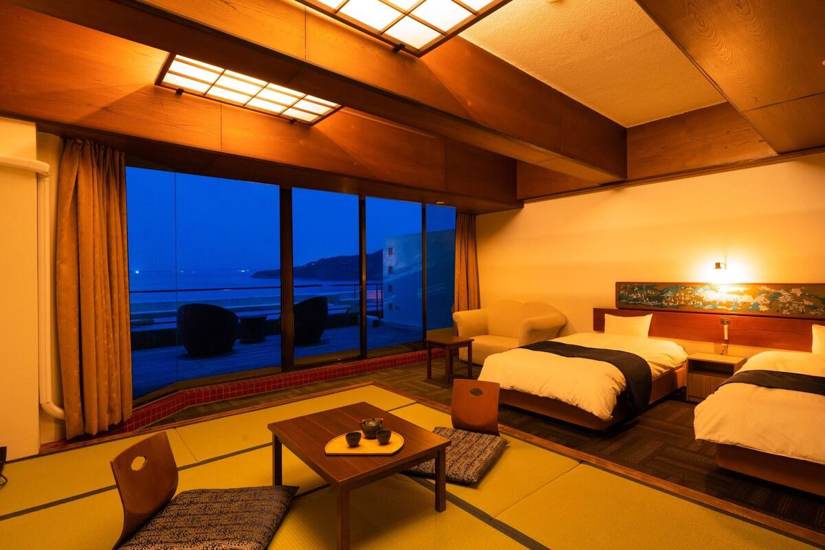 Une chambre d’hôtel avec deux lits, un canapé, une petite table avec une théière et une vue sur la mer.