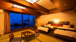 A hotel room with two beds, a sofa, a table with tea set, and a view of the sea. - Ooedo Onsen Monogatari Hotel Ranpu (Hirado)