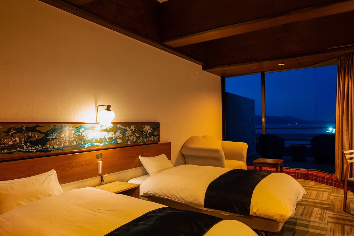 Une chambre d’hôtel avec deux lits, une table de chevet, une lampe, un tableau et une vue sur la mer.