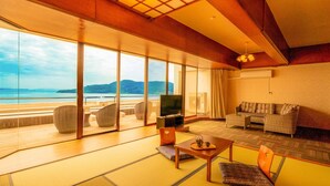 A spacious living room with a large TV, comfortable seating, and a view of the sea.