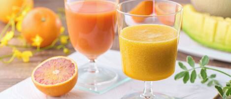 Two glasses of juice, one with a pinkish-orange liquid and the other with a yellowish-orange liquid, on a white napkin with a fruit cut in half and whole fruits in the background.