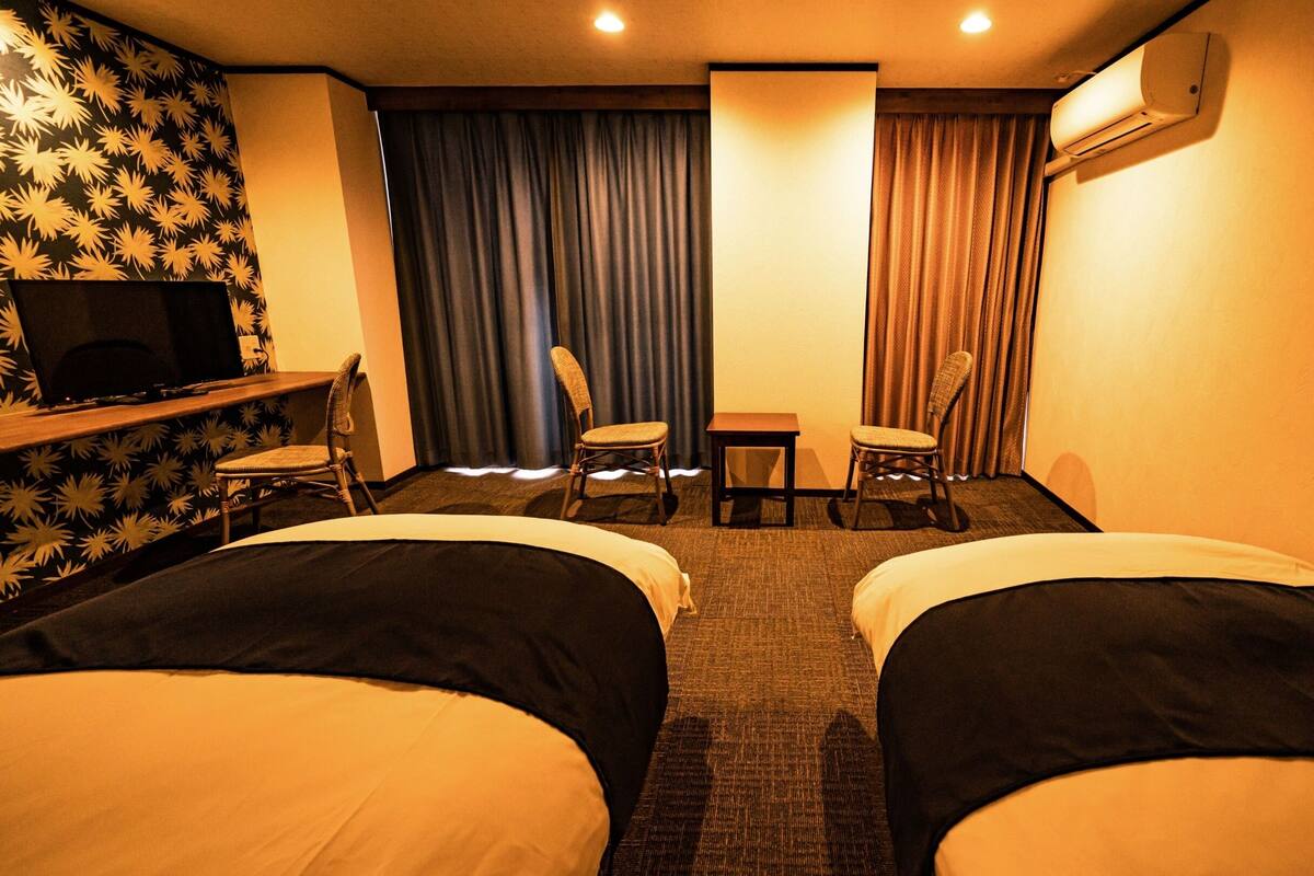 Une chambre d’hôtel avec deux lits, un bureau, une chaise, une télévision et un appareil de climatisation.