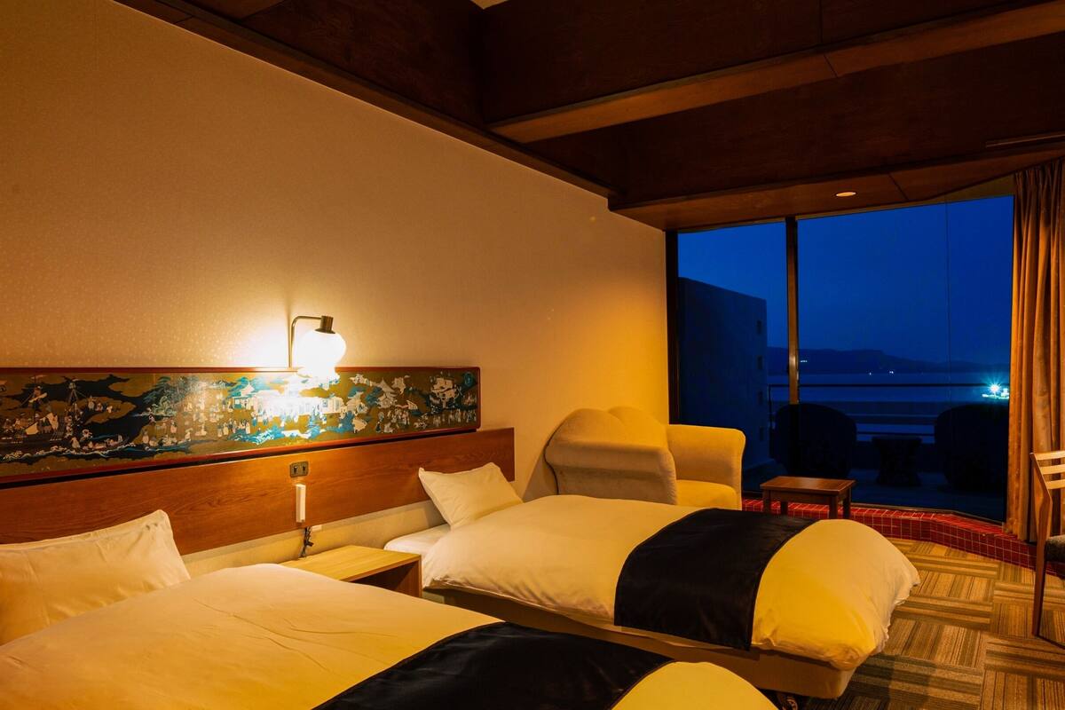 Une chambre d’hôtel avec deux lits, une table de chevet, une lampe, un tableau et une vue sur la mer.