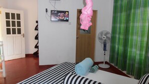 Una habitación con cama, televisión montada en la pared, ventilador y cortina verde a cuadros.