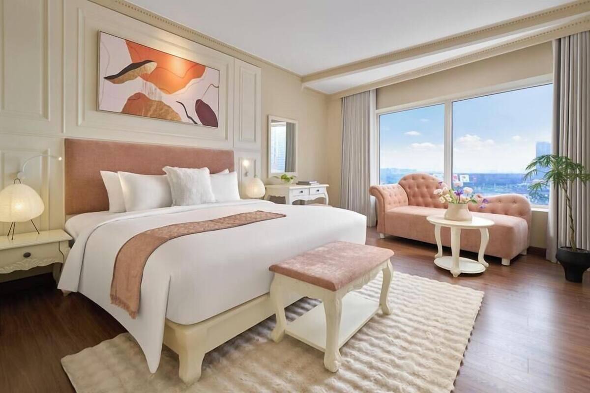 A spacious hotel room with a large bed, a sitting area, and a view of the city.
