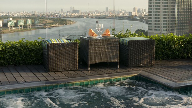 A waterfront terrace with wicker furniture and a view of a city skyline across the river. - Silverland Jolie Hotel (Ho Chi Minh City)