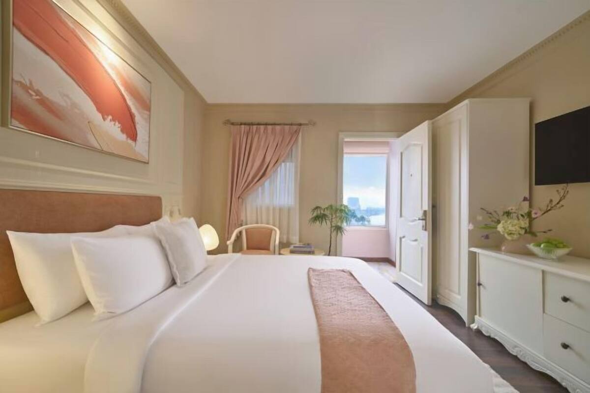 A hotel room with a large bed, a desk, a chair, a TV, and a window with curtains.