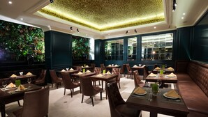 A restaurant with dark green walls, large windows, and a ceiling with a textured pattern. Tables are set with brown chairs, green napkins, and wine glasses. - Silverland Jolie Hotel (Ho Chi Minh City)