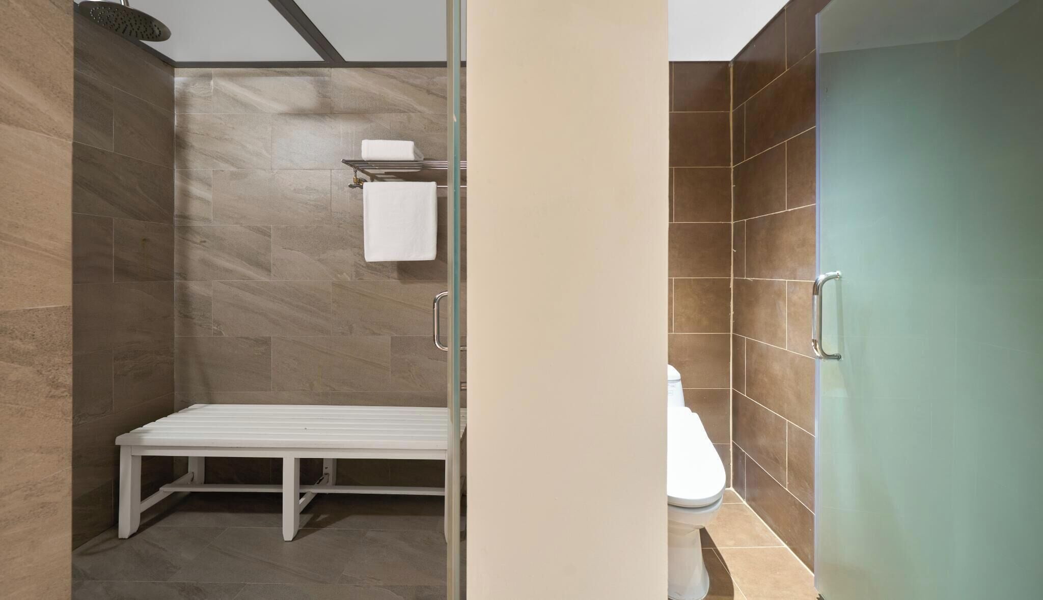 A modern bathroom with a bench, a toilet, and a shower area.