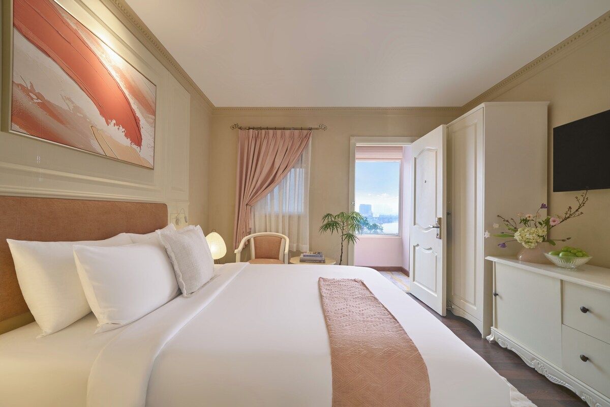 Une chambre d’hôtel avec un grand lit, un bureau, une chaise, une télévision et une fenêtre avec des rideaux.