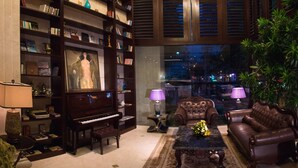 A well-lit living room with a piano, leather sofas, and a bookshelf filled with books and decorative items. - Silverland Jolie Hotel (Ho Chi Minh City)