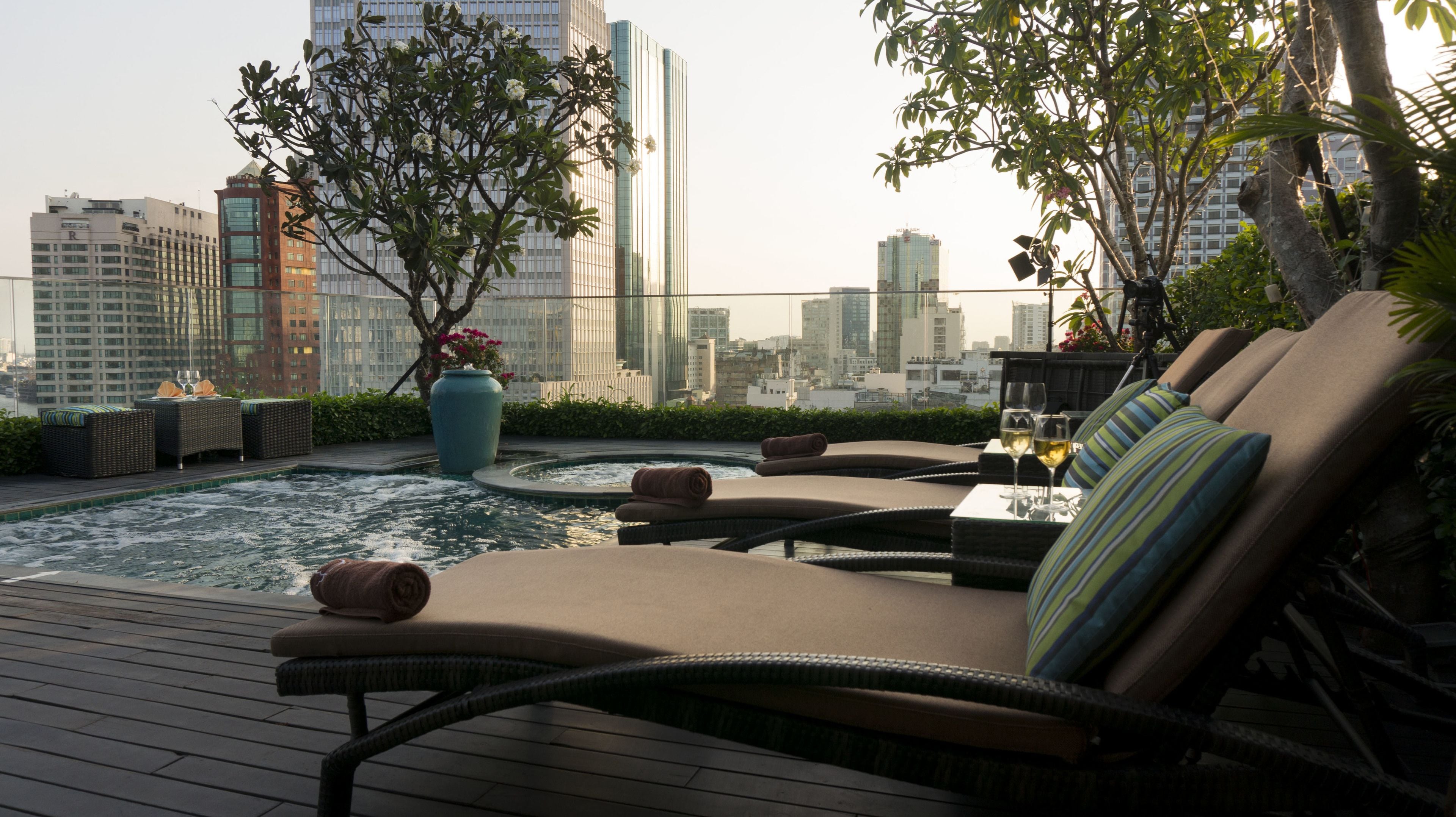 A rooftop lounge with a pool, lounge chairs, and a view of the city skyline.