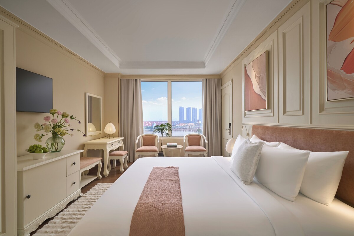 Une chambre d’hôtel spacieuse, dotée d’un grand lit, d’un bureau, de deux chaises, d’une petite table et offrant une vue sur de hauts immeubles.
