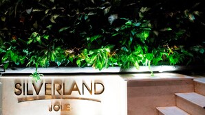 A stone bench with the inscription "SILVERLAND JOLIE" in front of a wall of green foliage. - Silverland Jolie Hotel (Ho Chi Minh City)