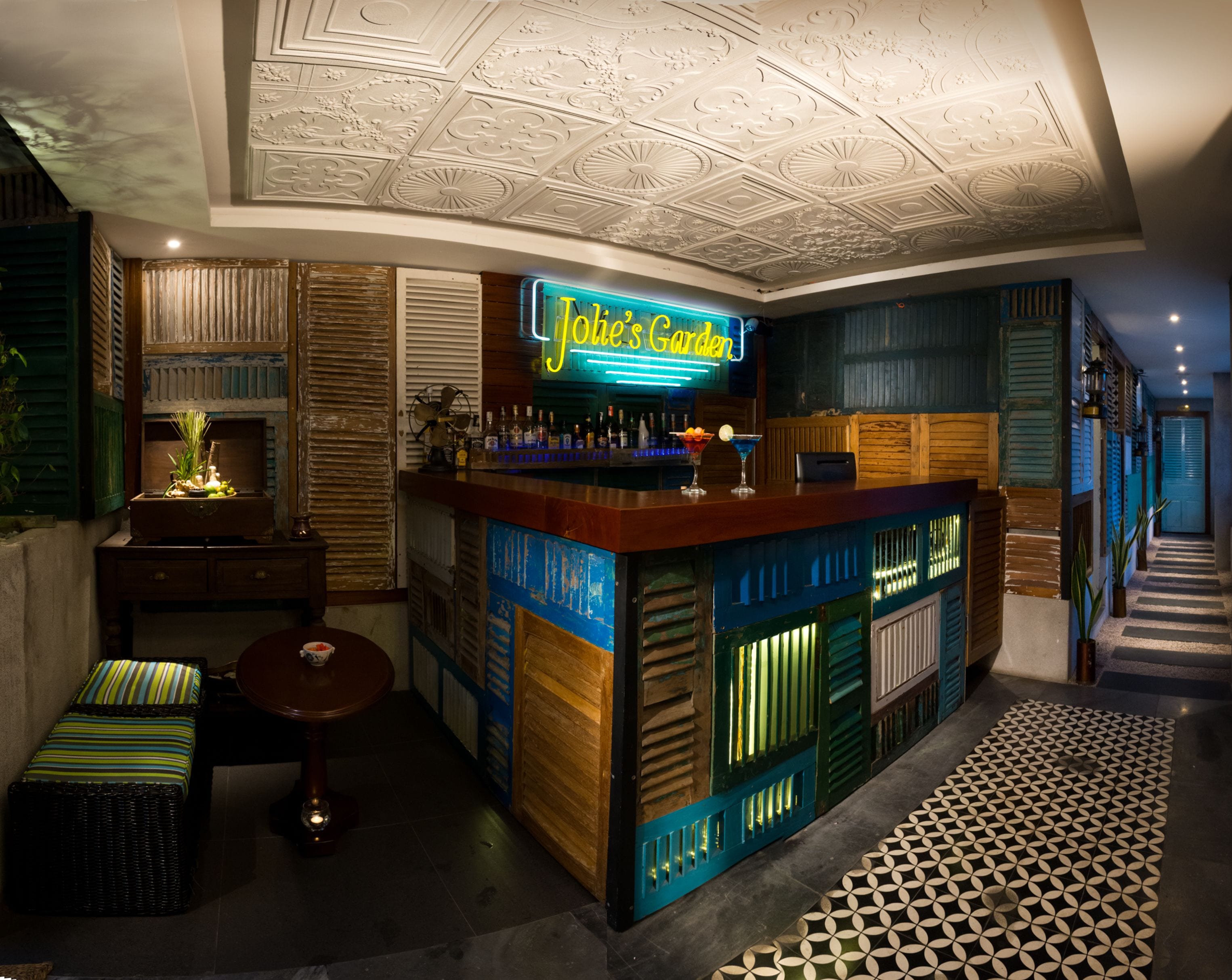 A bar area with a neon sign, wooden paneling, and a patterned floor.