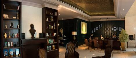 A spacious lobby with dark wood paneling, leather chairs, a fireplace, and a large green wall with framed pictures.