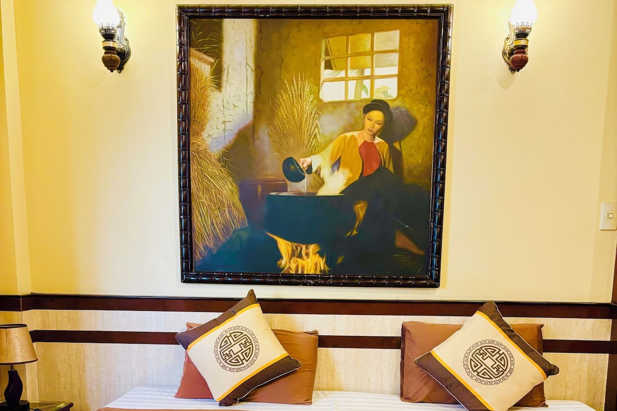 A hotel room with a large bed, two wall-mounted lamps, a framed painting, and a nightstand with a lamp.