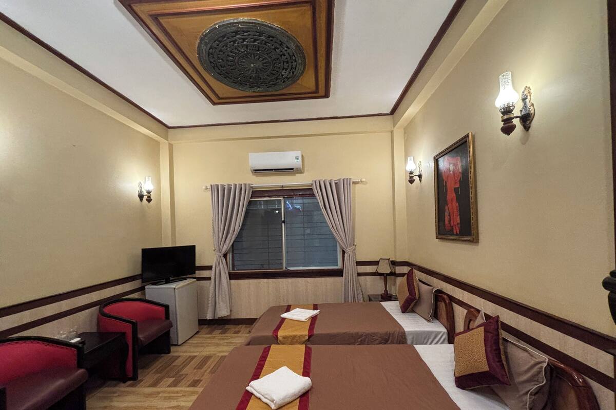 A hotel room with two beds, a TV, a desk, and a window with curtains.