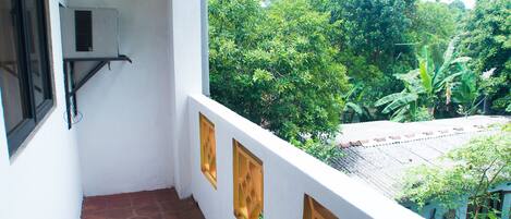 Un balcon avec un mur blanc, un sol carrelé de tuiles rouges et une vue sur une végétation luxuriante.