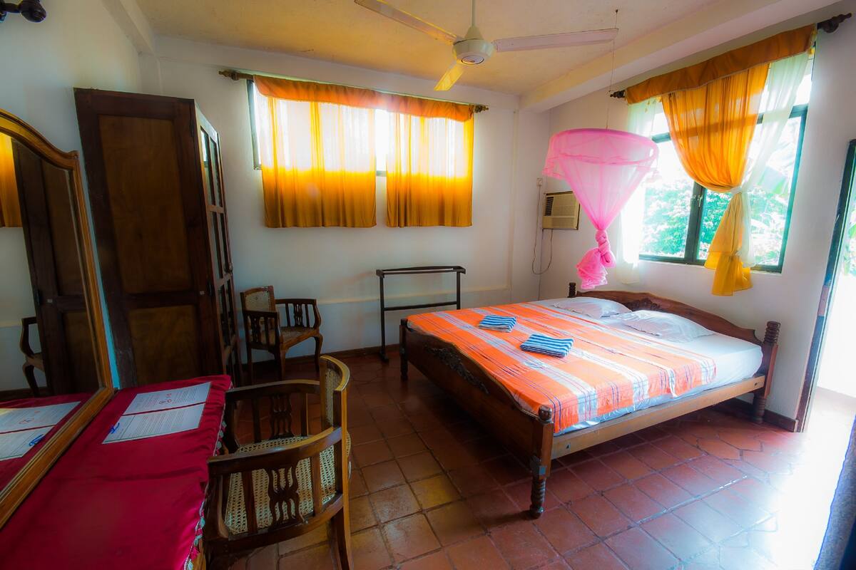 A room with a bed, a desk, a chair, a ceiling fan, and a window with curtains.