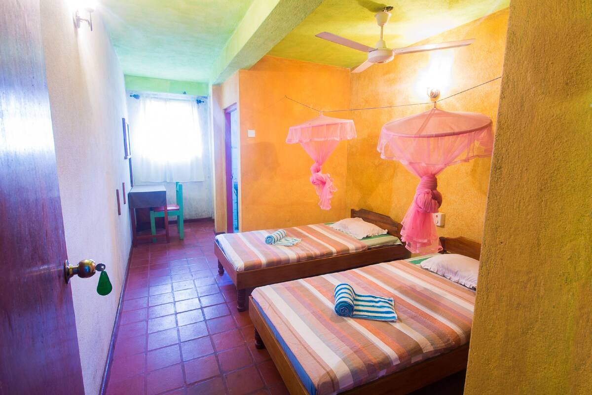 A room with two beds, a ceiling fan, and a window with curtains.