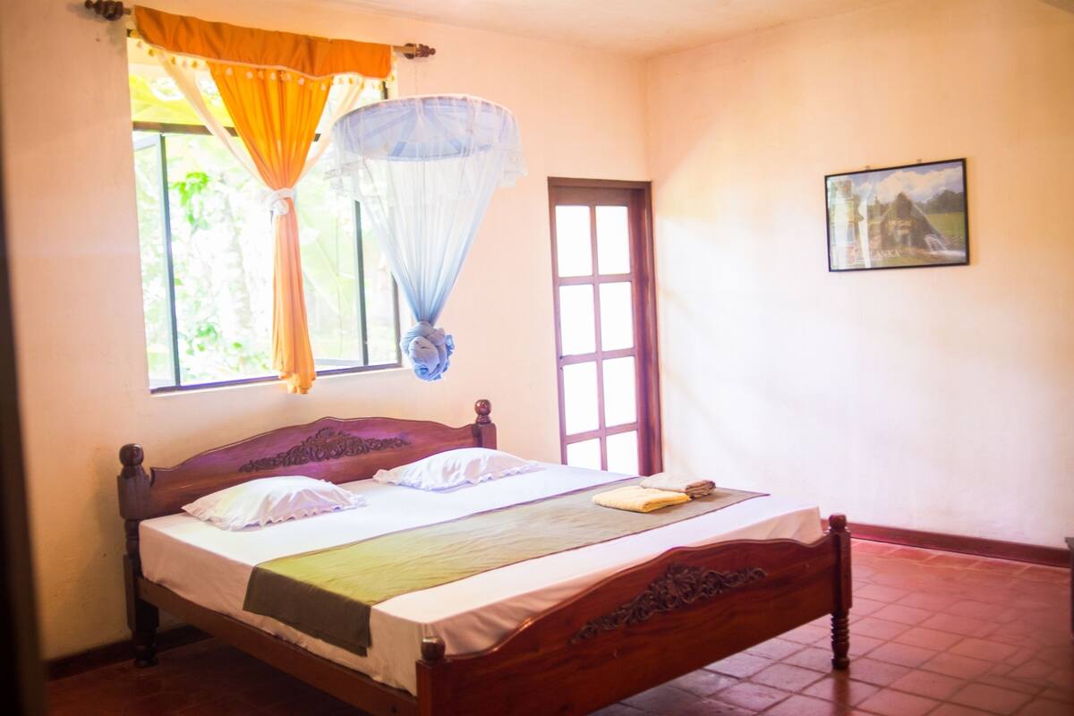 A bed with a wooden headboard, a mosquito net, and a window with curtains.