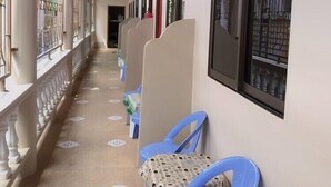 Un couloir bordé d’une rangée de chaises en plastique bleues et d’une table recouverte d’une nappe à motifs.