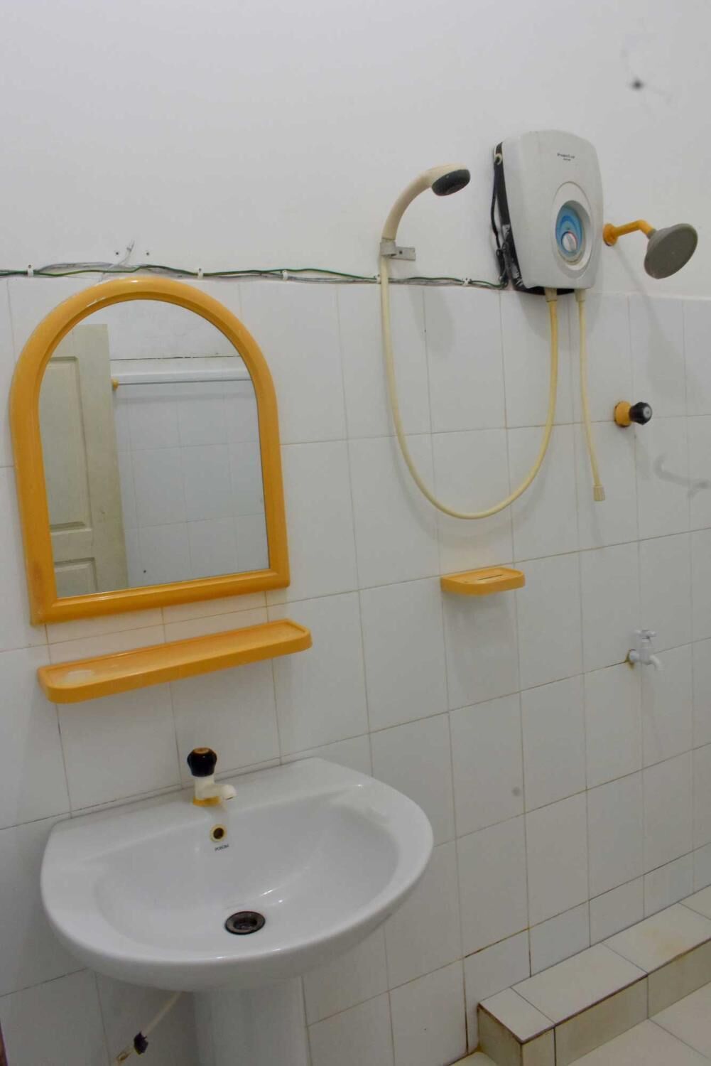 Une salle de bain avec un lavabo blanc, un miroir à cadre jaune, une douchette et un sèche-cheveux portatif.