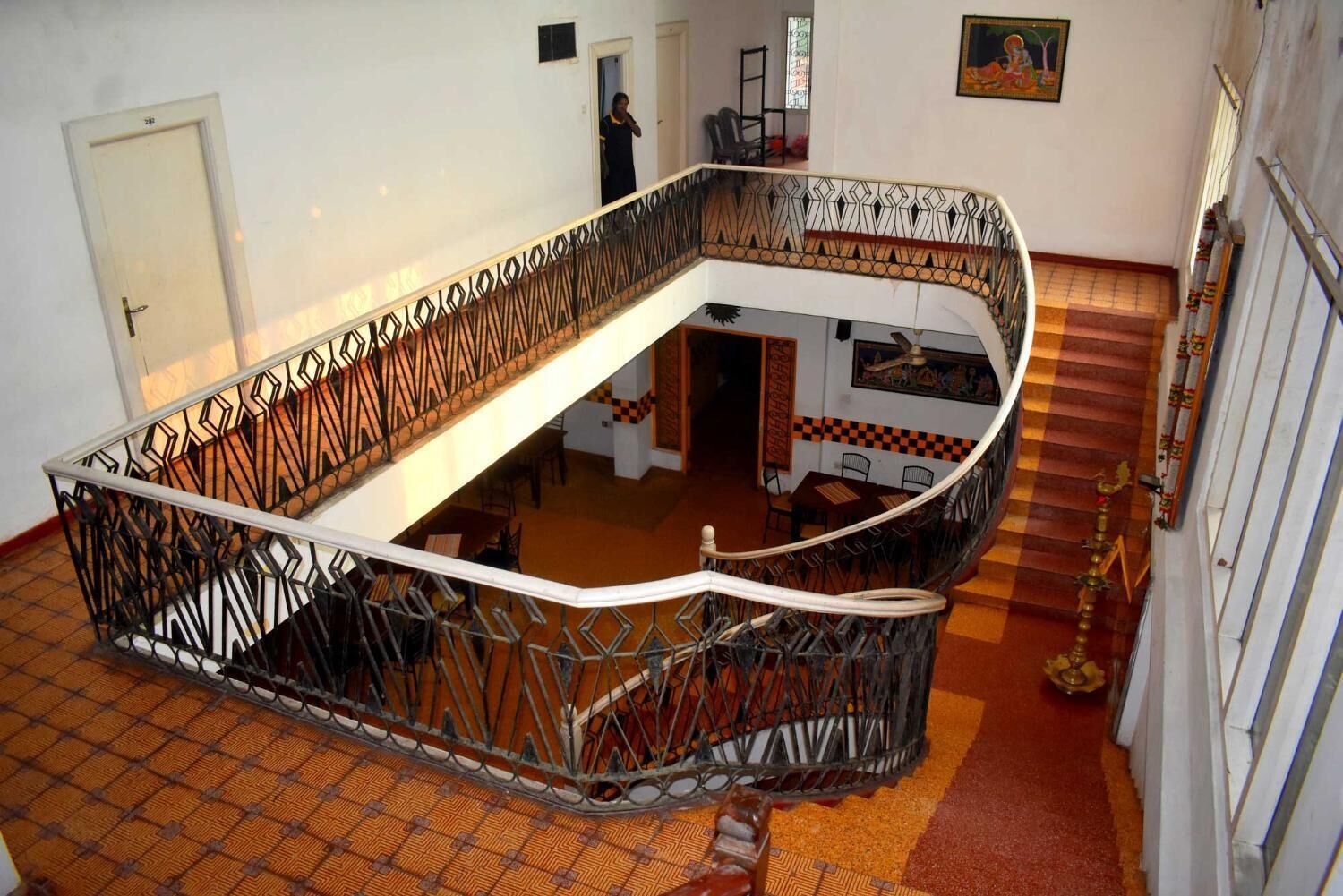 Un escalier en colimaçon orné d’une rampe en métal décorative, menant à un niveau inférieur doté d’un sol à carreaux et d’un coin repas.