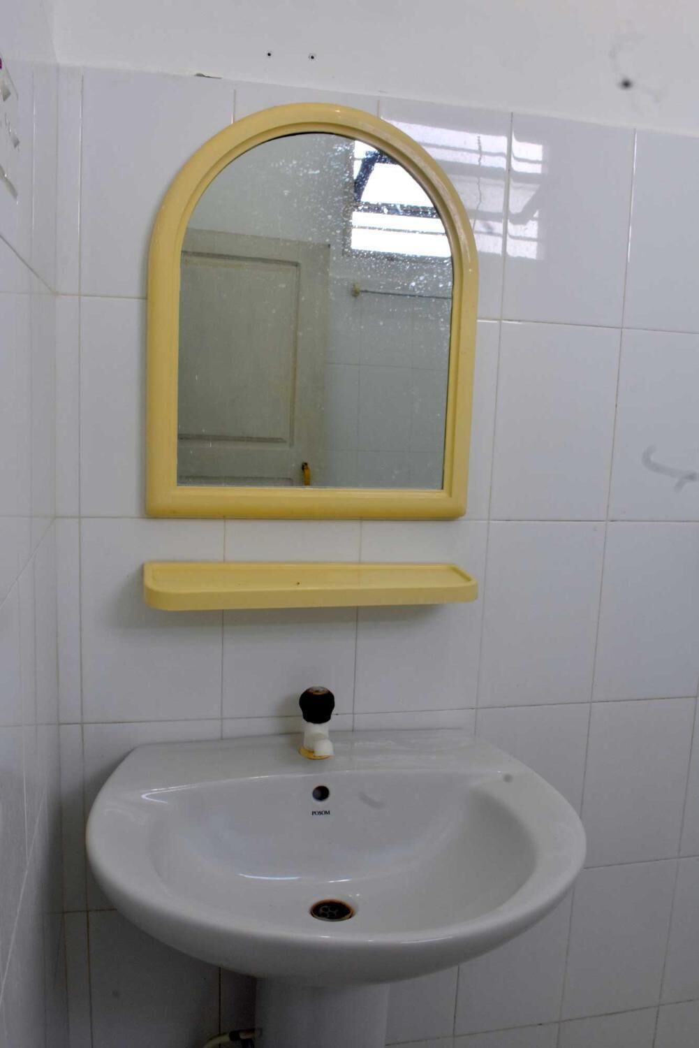 A bathroom with a white sink, a yellow-framed mirror, and a yellow shelf.